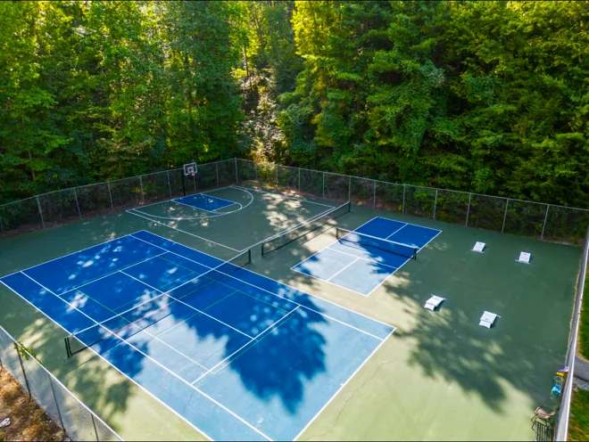 Aerial view of the Shagbark community courts: tennis, pickleball, a basketball half court and cornhole boards in a forest clearing